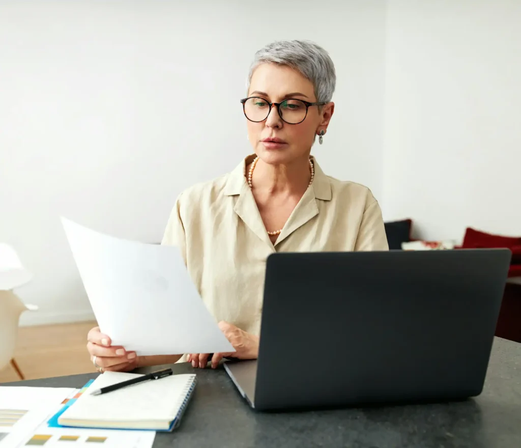 Kvinna som läser på att A4 papper framför dator