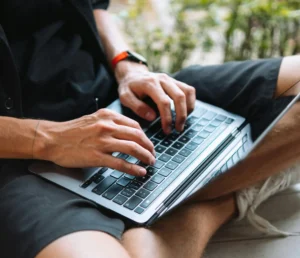 Man som sitter i skräddarställning med en dator i knät