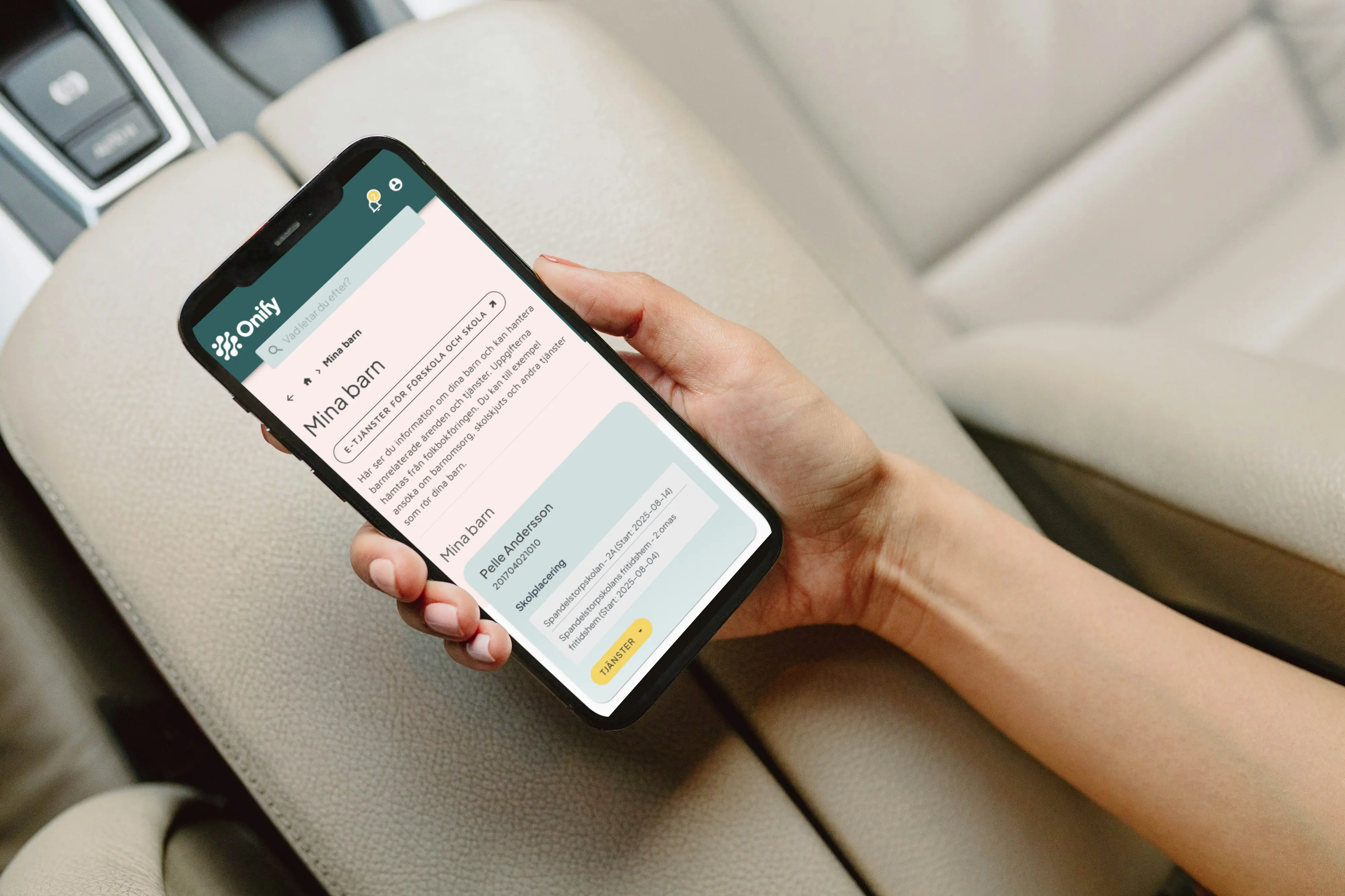 Bild visar en hand som håller i en mobil i en bil. Skärmen visar Onify Mina Barn.